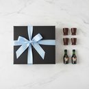 Baileys and dark chocolate shot glass gift set with double loop light blue satin bow on white marble surface